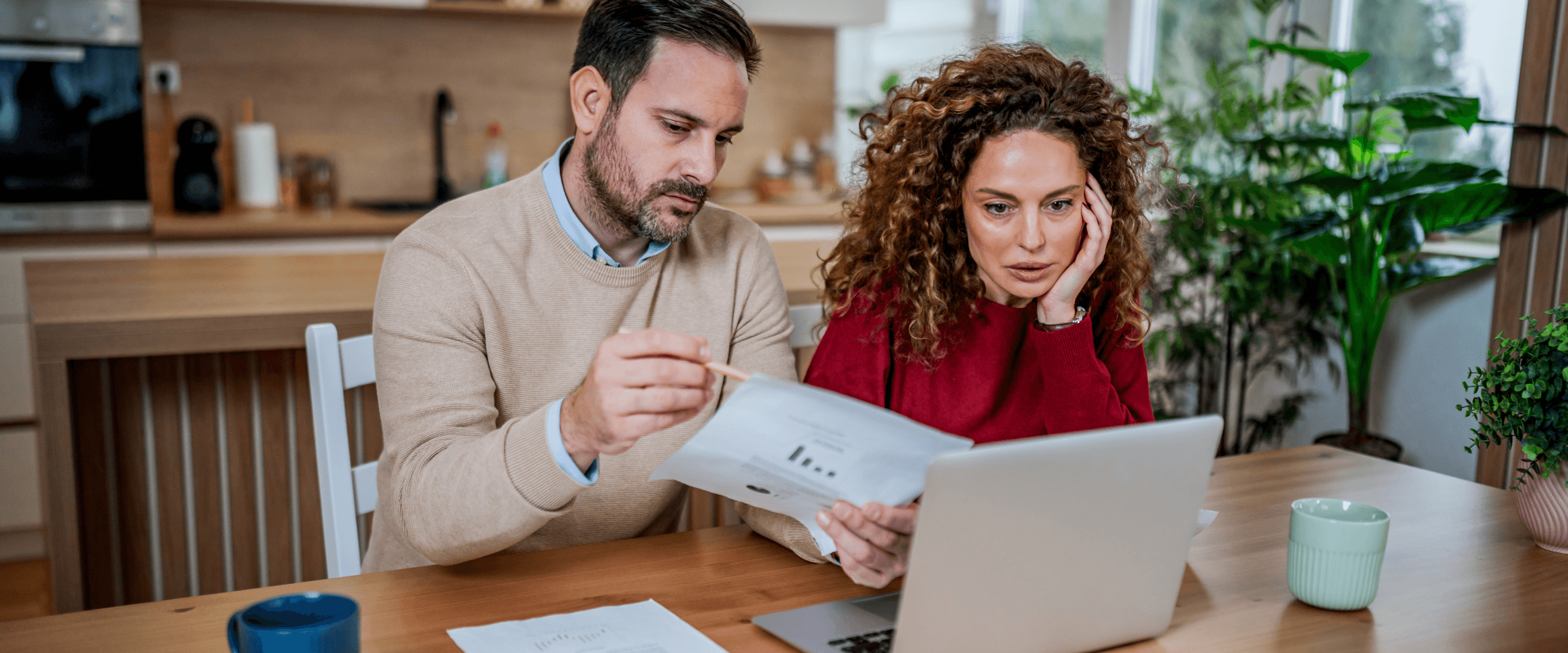 Couple at a kitchen table reviewing bills on a laptop while working out how much credit repair costs