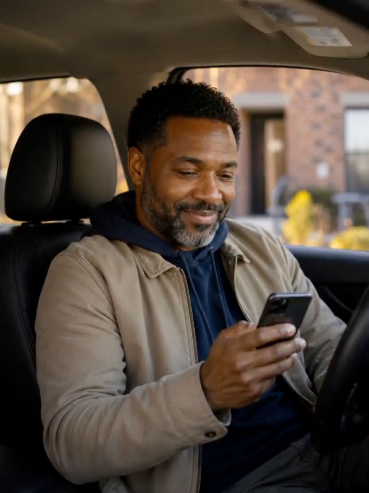 Man sitting in his car smiling at his phone