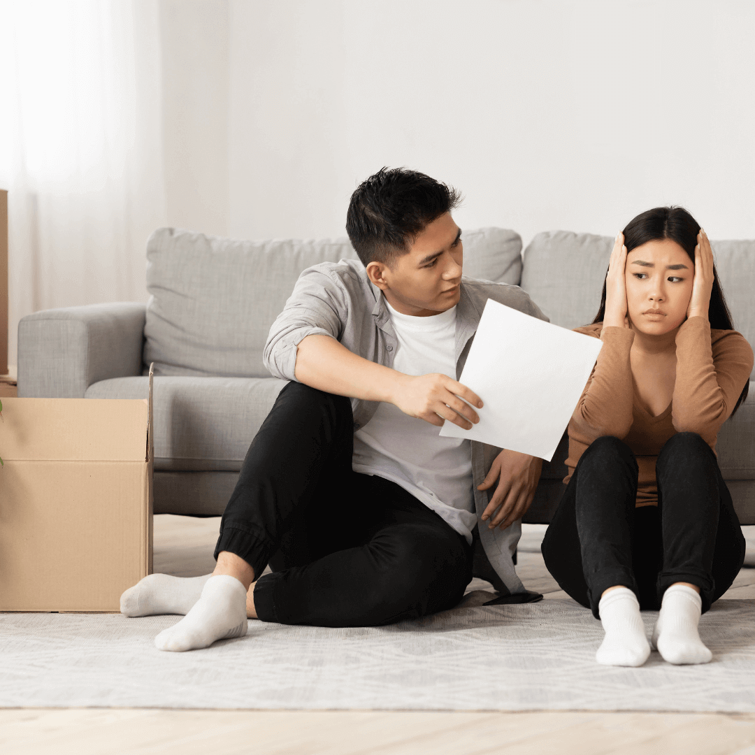 couple sitting on floor, looking at eviction notice, moving box next to them, visibly worried