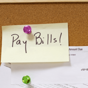 sticky note pinned to a board that says Pay Bills! with a payment statement behind it.